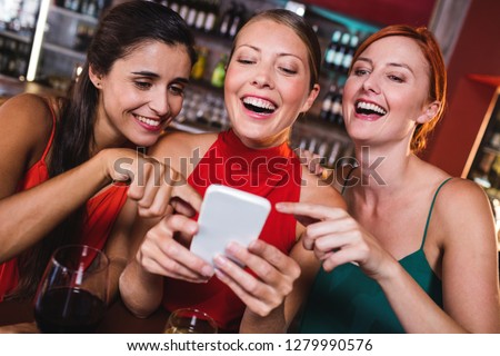 Female friends using mobile phone while enjoying wine in night club