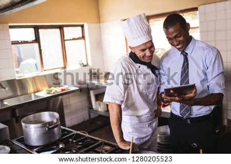Male manager and chef using digital tablet in kitchen at hotel