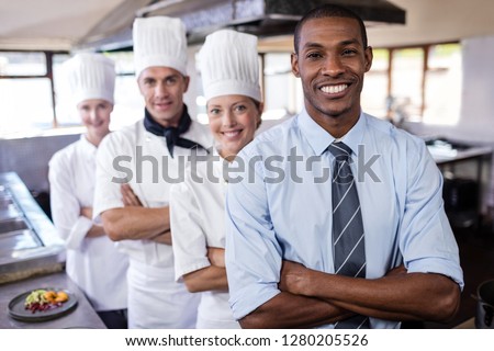 Group of diverse chefs and manager standing with arms crossed in kitchen at hotel