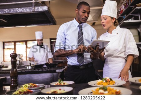 Male manager and female chef using digital tablet in kitchen at hotel
