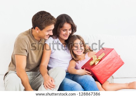 Parents offering a gift to their daughter on a sofa
