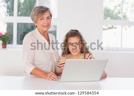 Grandmother and child looking at camera together with laptop in kitchen