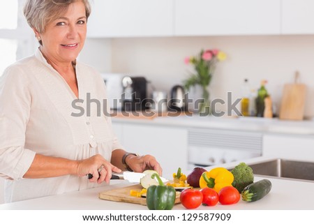 Elderly woman cutting vegetables on a cutting board with a smile in kitchen