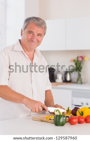 Old man smiling and chopping vegetables in kitchen