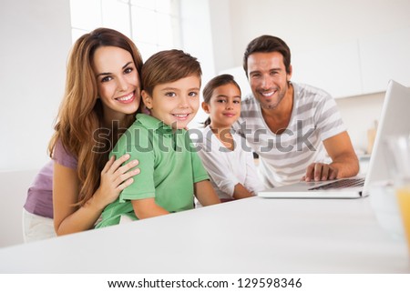 Happy family looking at the camera with a laptop in kitchen Happy family looking at the camera with a laptop in kitchen