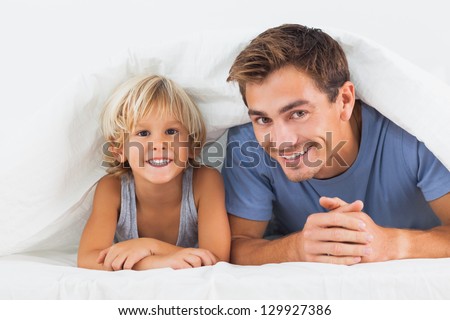 Father and his son lying under the duvet on the bed