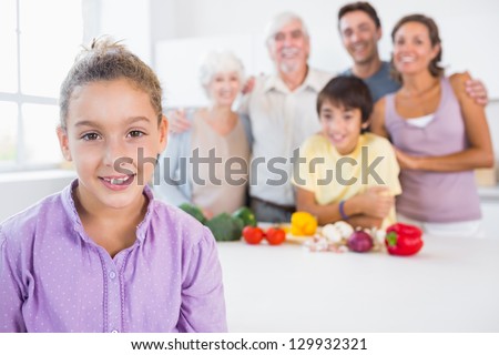 Young girl standing beside kitchen counter with family behind her