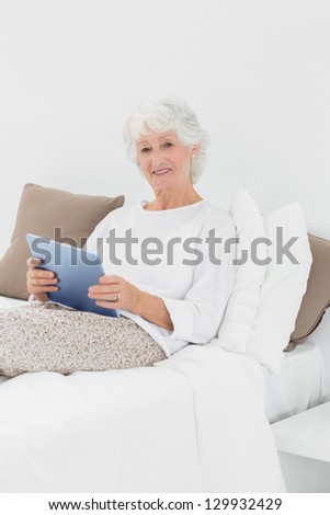 Cheerful elderly woman using a digital tablet on the bed