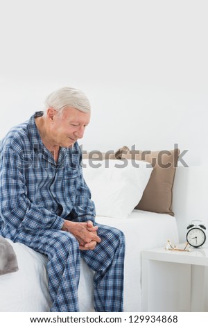 Calm elderly man sitting on the bed in the bedroom