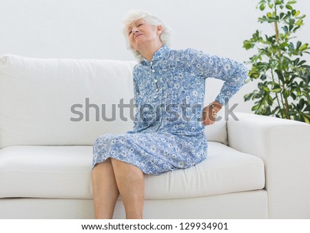 Elderly woman suffering with back pain on a sofa