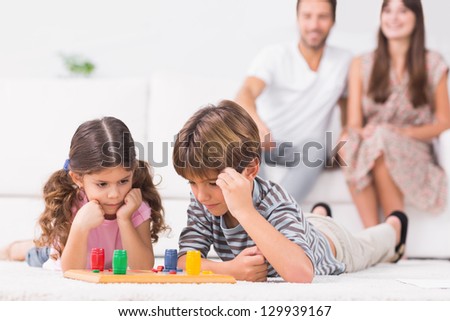 Siblings playing board game on the floor with parents sitting behind them