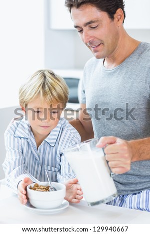 Father pouring milk onto sons cereal at breakfast