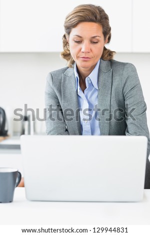Woman in suit using laptop in kitchen