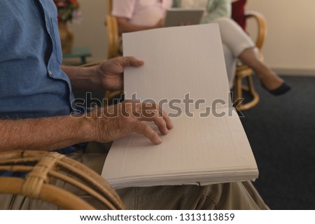 Mid section of blind senior man reading a braille book at nursing home