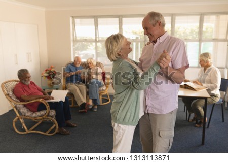 Side view of active senior couple dancing with senior people reading at nursing home