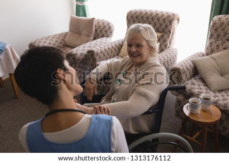 Rear view of female doctor interacting with disabled senior woman in living room at nursing home