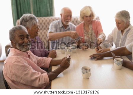 Front view of group of senior people playing cards around table in living room at nursing home