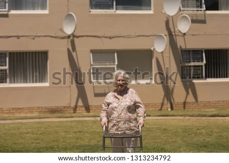 Front view of happy disabled senior woman walking with walker on sunny day in garden