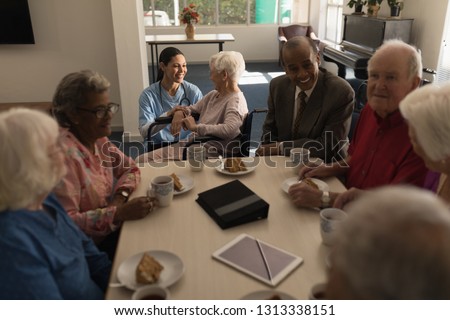 Front view of group of senior friends having breakfast on dining table at nursing home