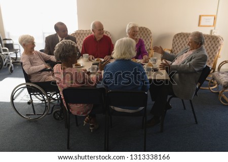 Front view of group of happy senior friends having breakfast on dining table at nursing home