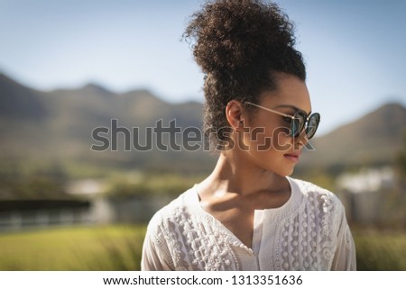 Close-up of young mixed race woman with sunglasses looking to the side while standing in backyard of her home on a sunny day