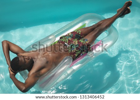 High angle view of young African American man with hands behind head relaxing on pool lounger in swimming pool