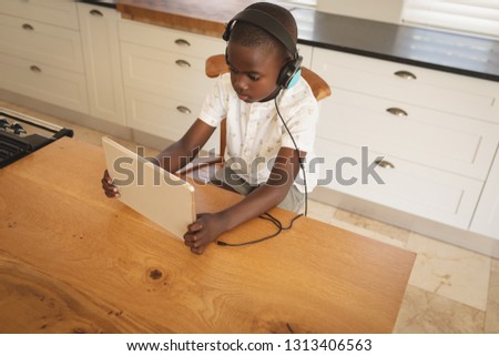 High angle view of African American boy playing game on digital tablet at dining table in kitchen at home