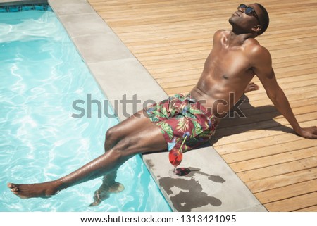 Side view of young African American man sitting at poolside in his backyard on a sunny day