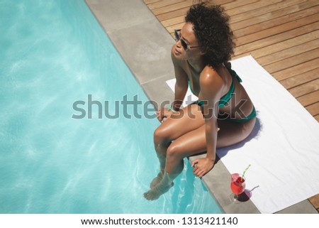High angle view of beautiful young African American woman sitting at poolside in her backyard on a sunny day