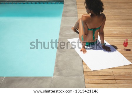 Rear view of young African American woman relaxing at poolside in her backyard on a sunny day