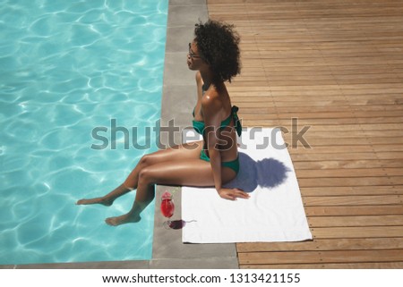 Side view of beautiful young African American woman sitting at poolside in her backyard