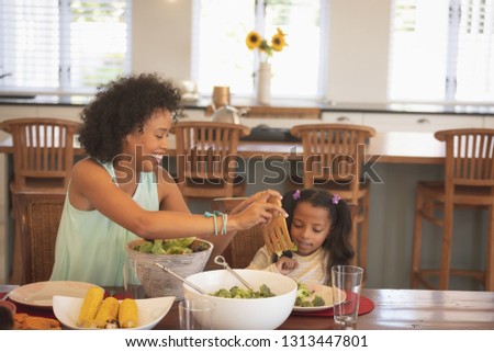 Front view of African American mother serving salad to her daughter at dining table in a comfortable home