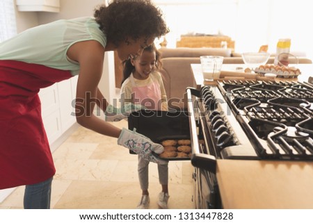 Side view of African American mother and daughter taking freshly baked cookies from the oven in the kitchen at home