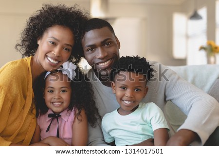 Front view of happy African American family sitting on sofa and looking at camera in a comfortable home
