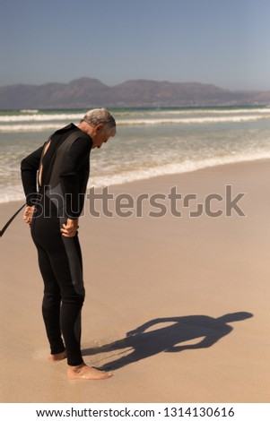 Side view of senior male surfer wearing wet suit on the beach with mountains in the background