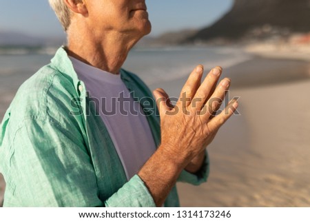 Mid section of senior man praying with eyes closed on the beach