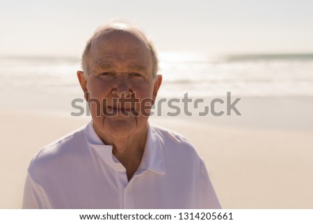 Front view of smiling senior man looking at camera on beach in the sunshine
