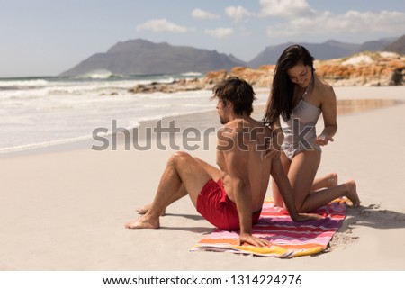 Front view of beautiful happy young woman applying sunscreen lotion on mans back at beach in the sunshine