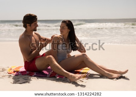 Side view of happy young man applying sunscreen lotion on woman back at beach in the sunshine
