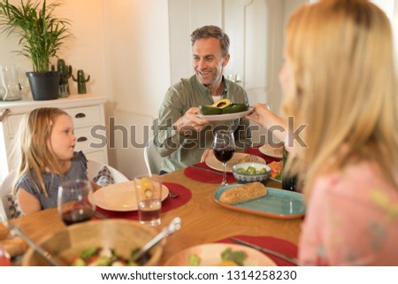 Rear view of a woman passing food to man on dining table at home