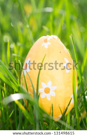 Orange easter egg nestled in the grass in the sunshine