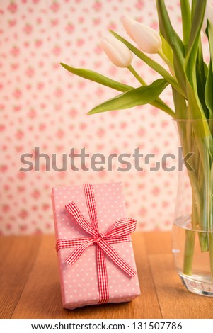 Vase of tulips on wooden table with pink wrapped gift and wallpaper background
