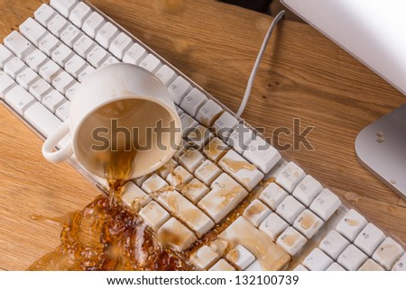 Cup of tea spilling over a keyboard on a desk