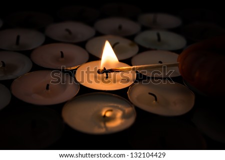 Match lighting tea light candle with others unlit