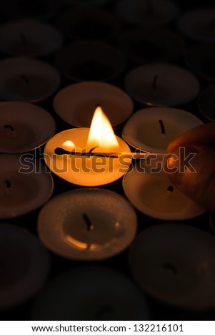 Hand lighting tea light candle with match in the darkness