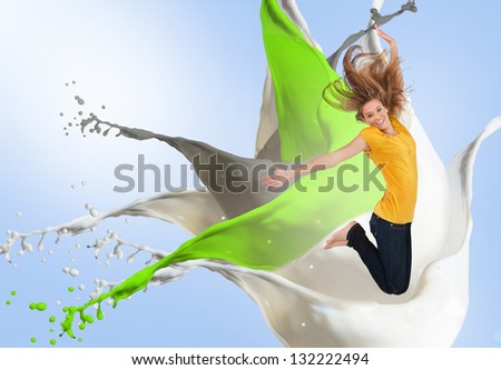Pretty young woman jumping for joy with artistic green white and grey paint splashes on blue background