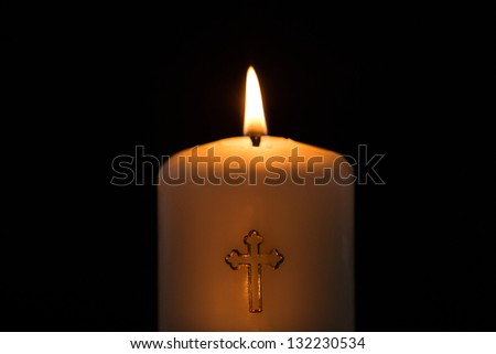 Candle with golden cross embellishment burning on black background