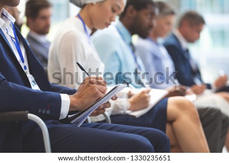 Mid section of Caucasian businessman writing on notepad during seminar in office building