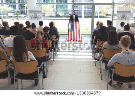 Front view of male mixed race speaker speaks in a business seminar in office building with american flag