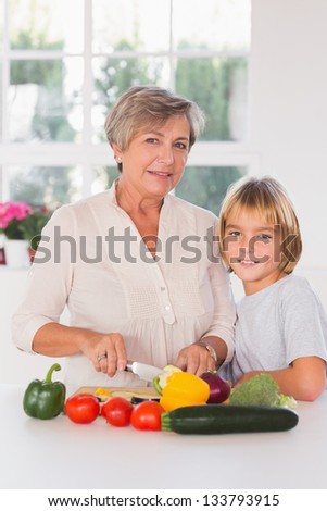 Granny cutting vegetables with her grandson in kitchen
